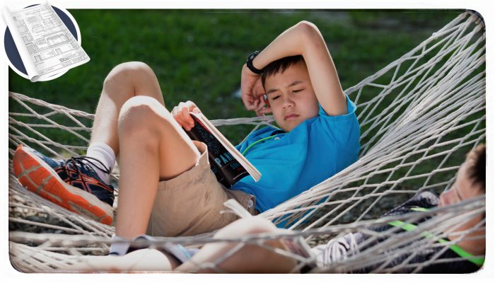 A boy reading a book in a hammock.